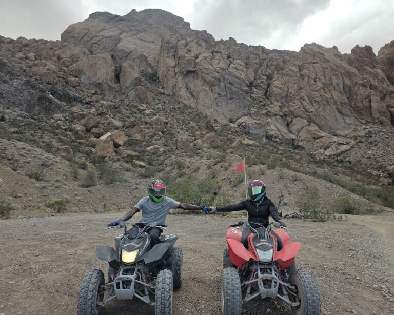 Couple on black and red ATVs hold hands in Nevada’s rocky desert near Las Vegas on an exciting ATV tour adventure.