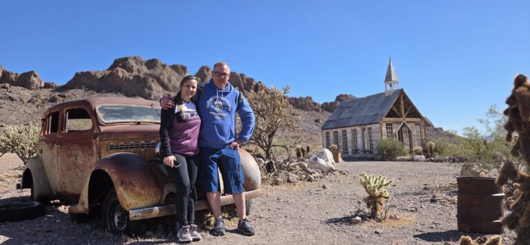 Smiling couple by a rusty vintage car in a Nevada desert ghost town near Las Vegas, perfect for ATV tours and sightseeing.