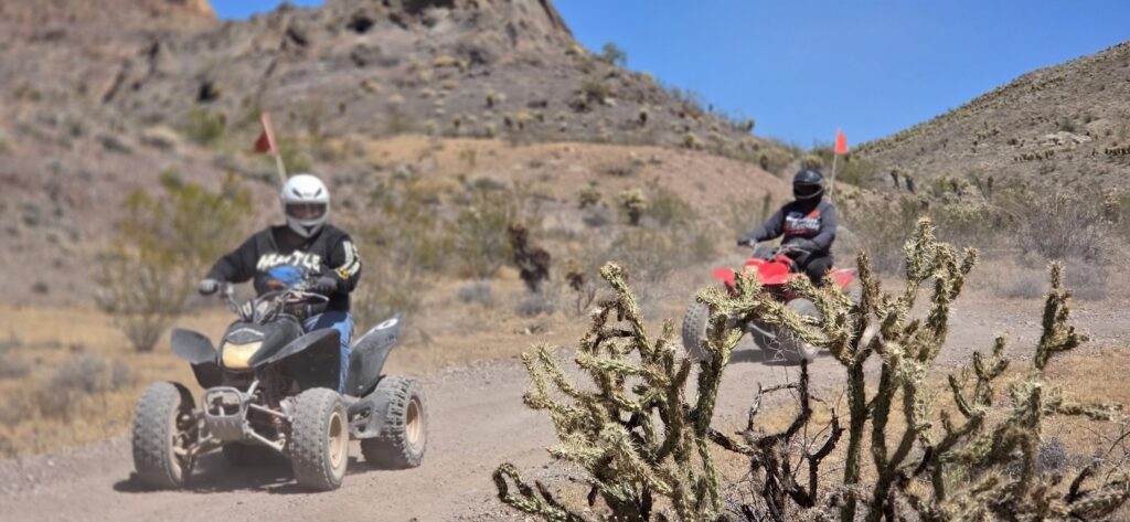 ATV riders explore a dusty desert trail near Las Vegas, Nevada, with rocky hills, cactus, and blue sky—perfect for an ATV tour.
