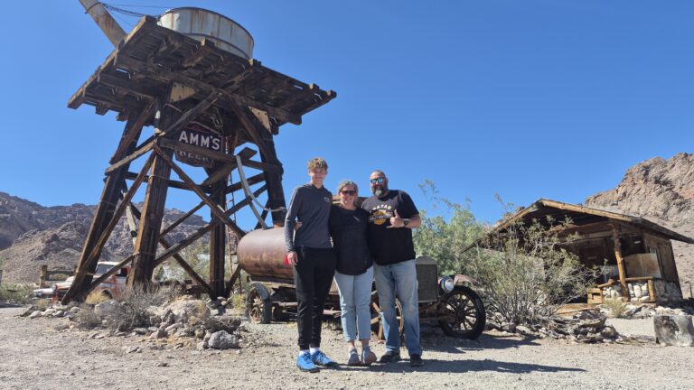 Smiling friends in front of Nevada ghost town mining ruins and water tower near Las Vegas, perfect for ATV tours and sightseeing.