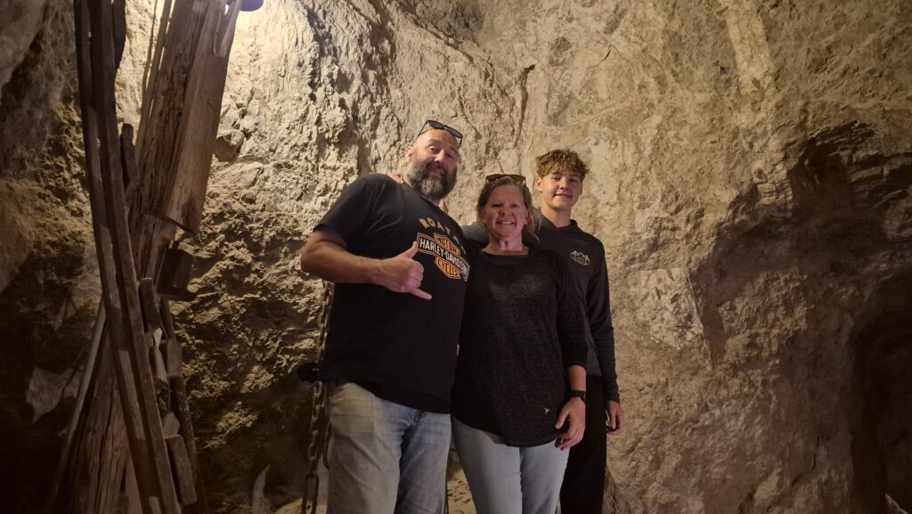 Three people smile in a rocky Nevada cave near the Colorado River, enjoying ATV tours and Ghost Town sightseeing.