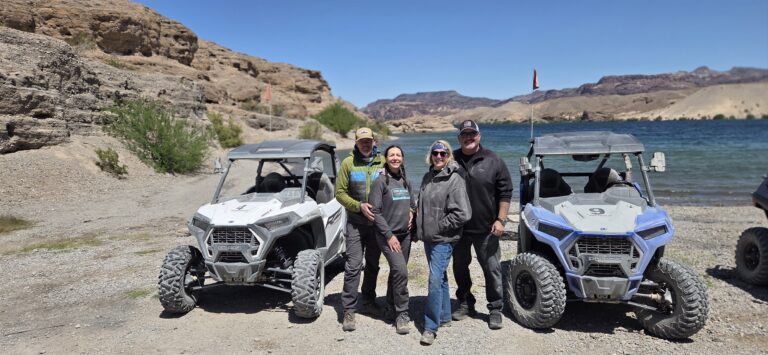 Group smiles on rocky Colorado River shore near Las Vegas, standing by RZRs after an exciting Nevada ATV tour adventure.