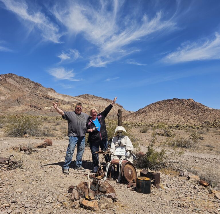 Smiling visitors pose by a mannequin in Nevada desert near Las Vegas, with mining relics—perfect for Ghost Town sightseeing.