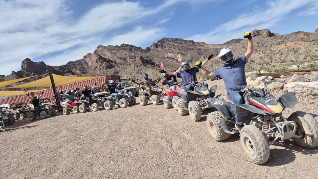 Adventurers on a Las Vegas ATV tour ride dusty desert trails near Nevada’s rocky mountains, arms raised in excitement.