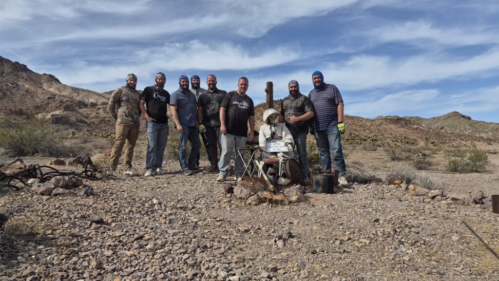 Group of 8 smiling in Nevada desert near Las Vegas, with prospector mannequin; ideal for Ghost Town sightseeing or ATV tours.
