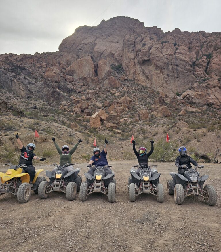Group enjoying an ATV tour near Las Vegas, Nevada, raising arms with rocky mountains and cloudy skies in the background.