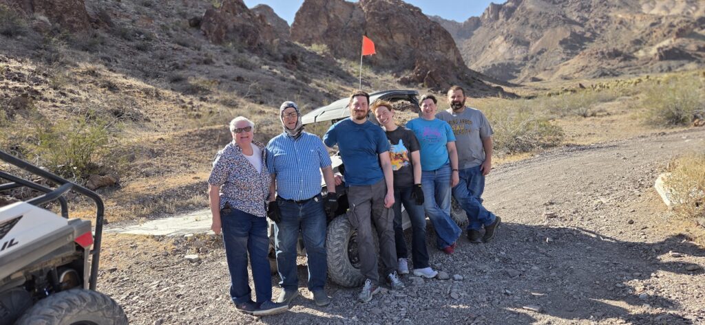 Group stands on a rocky Nevada trail by an off-road vehicle, with Las Vegas desert hills; perfect for ATV or RZR adventure tours.