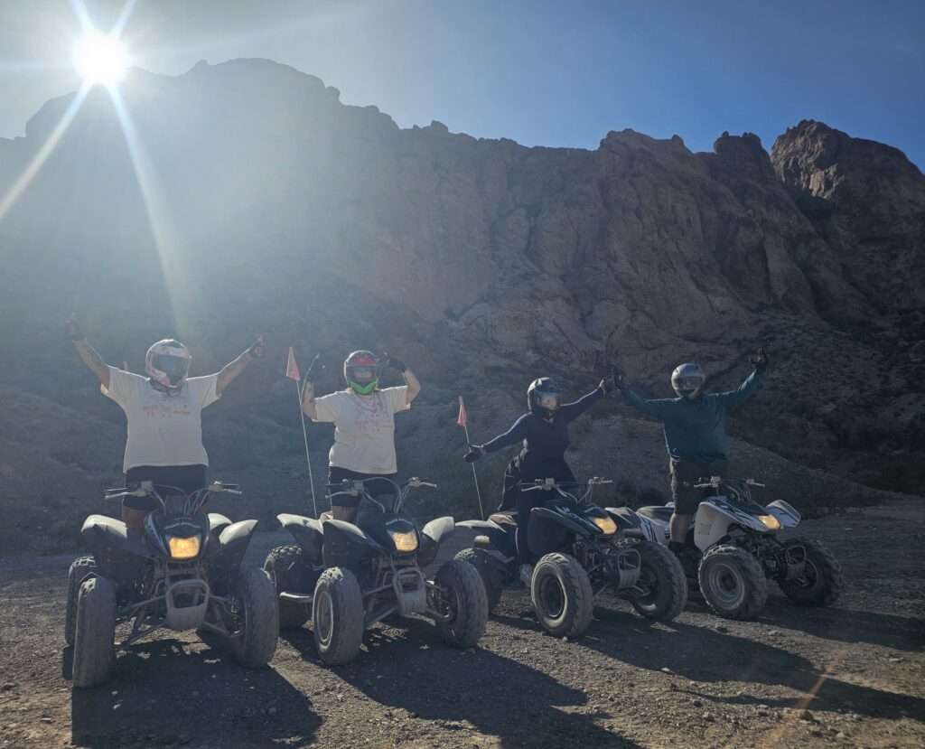 Adventurers on ATVs in Nevada near Las Vegas, enjoying an exciting RZR off-road tour with sunlit mountains and a clear blue sky.