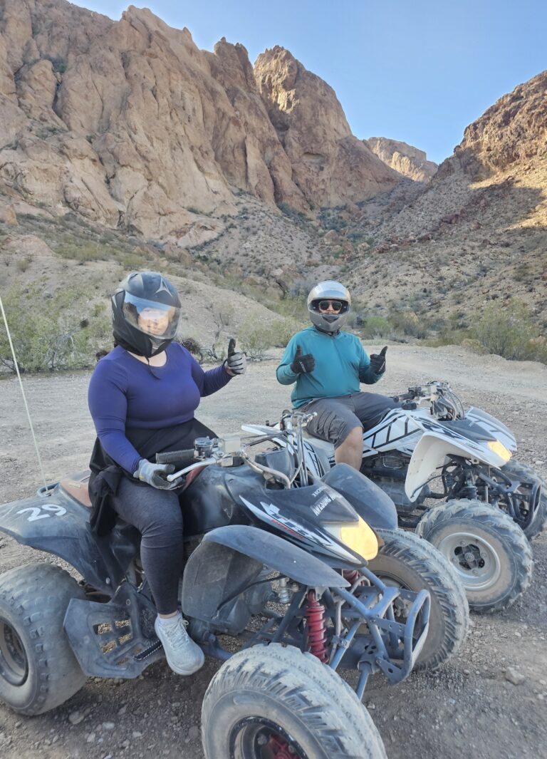Two riders on black ATVs give thumbs up on a Nevada desert trail near Las Vegas, perfect for ATV tours and off-road adventures.