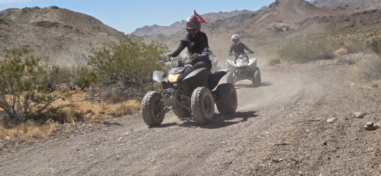 Adventurers enjoy an ATV tour on a dusty Nevada desert trail near Las Vegas with mountains and sparse vegetation in view.