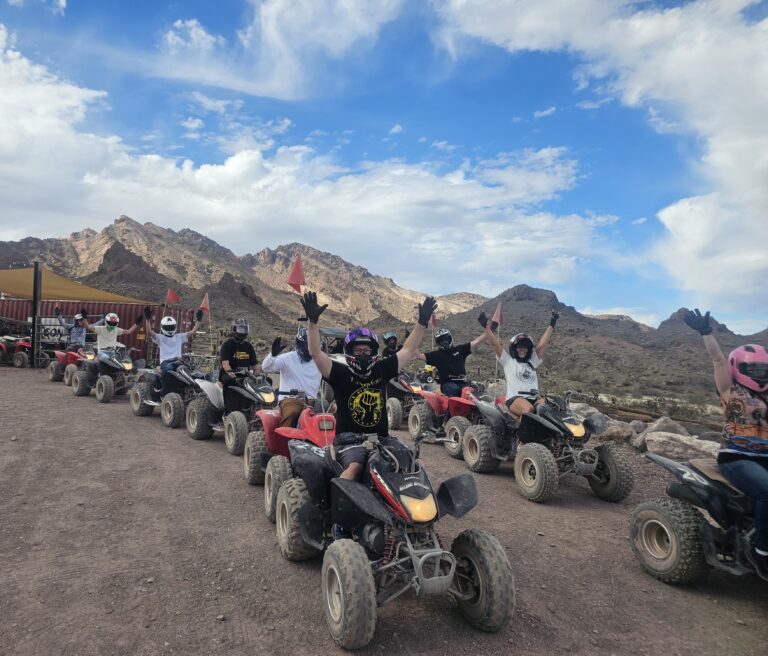 Adventurers on an ATV tour near Las Vegas, Nevada ride along a desert trail with mountains and blue sky in the background.