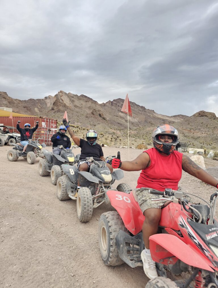 Group on ATVs giving thumbs up during a Nevada desert ATV tour near Las Vegas with rocky mountains in the background.