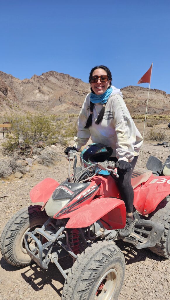 Smiling woman on red ATV in Nevada desert near Las Vegas, mountains behind, perfect for ATV tours or Ghost Town sightseeing.