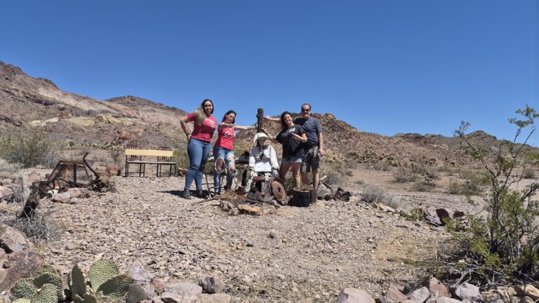 Group poses by a mannequin in Nevada’s rocky desert near Las Vegas, with rusted gear and mountains, perfect for Ghost Town tours.