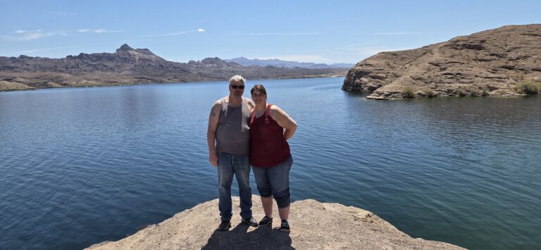 Couple on rocky ledge overlooking Colorado River near Las Vegas, Nevada, mountains in background, blue sky—perfect for ATV tours.