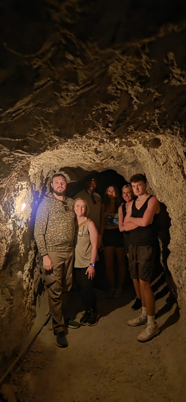 Six people pose in a dim cave tunnel near the Colorado River, Nevada—smiling after a Las Vegas ATV tour adventure.