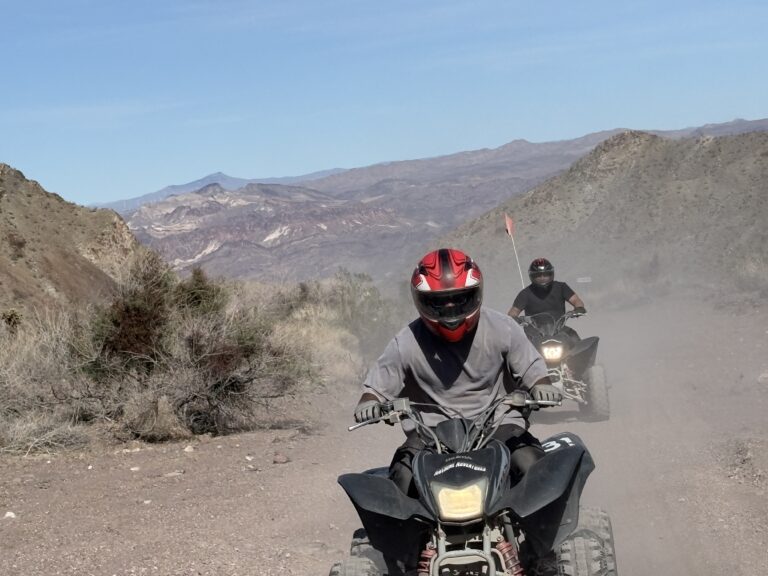 ATV riders on a dusty Nevada desert trail near Las Vegas, with rocky mountains—ideal for ATV tours and off-road adventures.