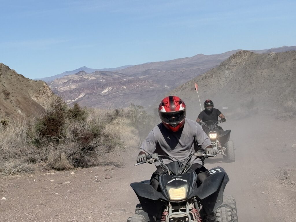 Adventurers on an ATV tour ride through Nevada’s rocky desert near Las Vegas, mountains and blue sky in the background.