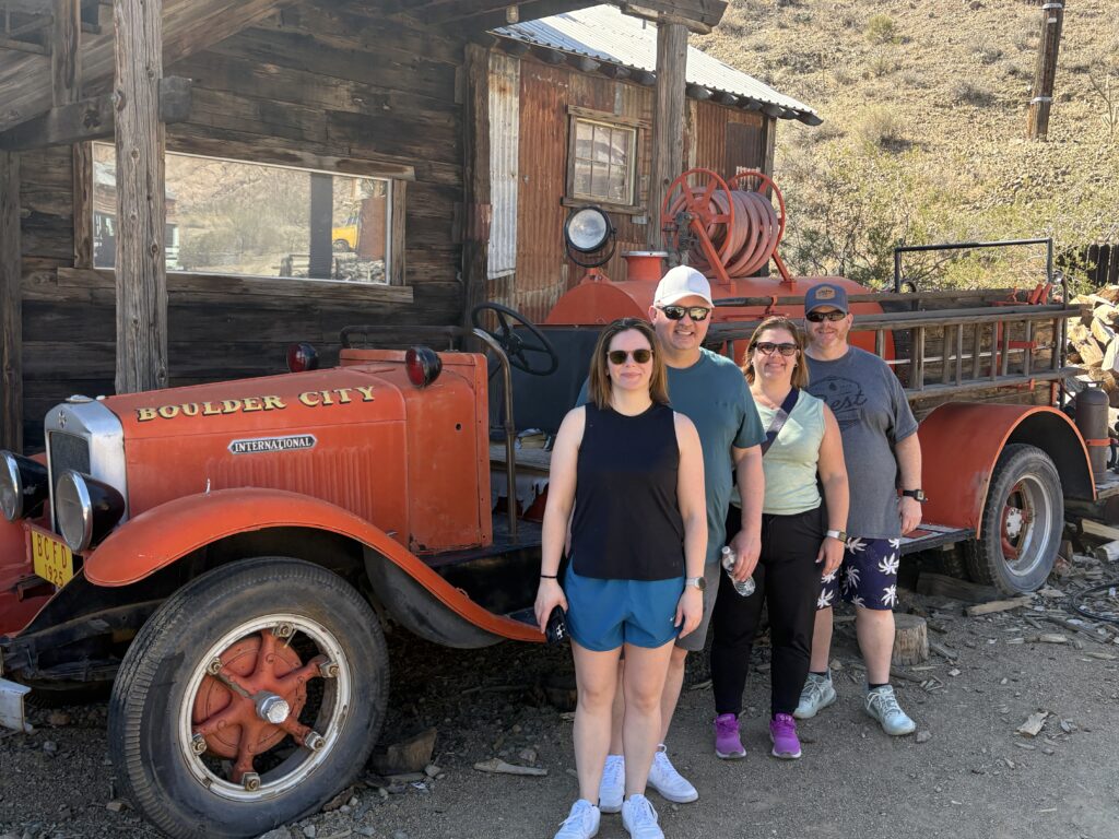 Smiling friends pose by a vintage Boulder City fire truck in Nevada near Las Vegas—perfect for Ghost Town sightseeing adventures.