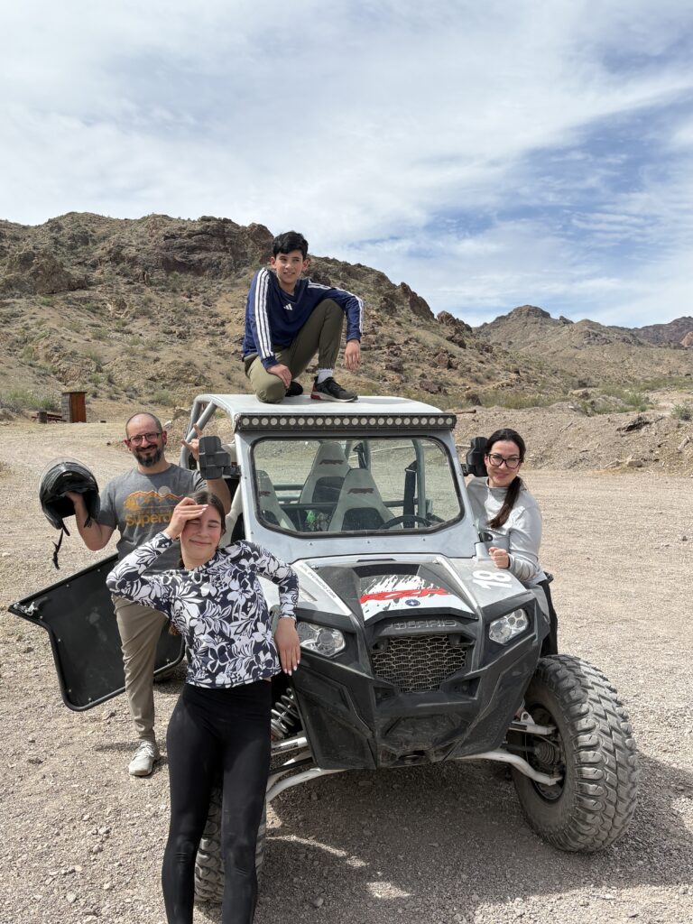 Group poses with off-road vehicle in Nevada desert near Las Vegas, ready for an exciting RZR ATV tour adventure.