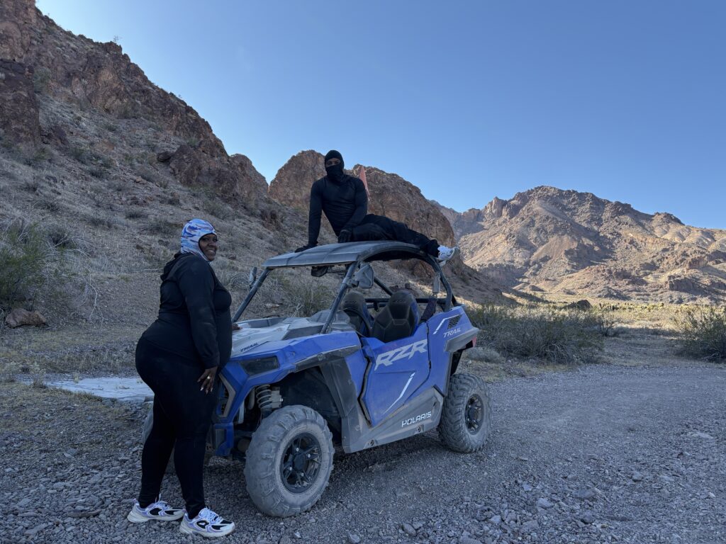 Two people on a blue ATV during an exciting Nevada RZR tour, posing on a rocky desert trail near Las Vegas and the Colorado River.
