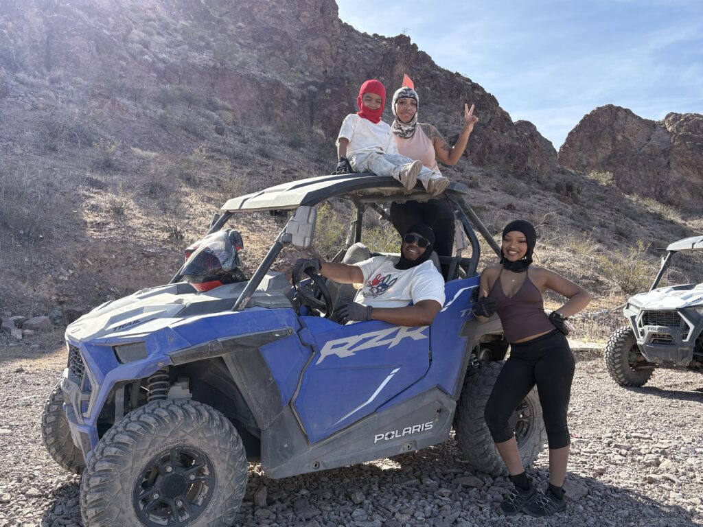 Group in helmets pose with a blue Polaris RZR during an ATV tour near Las Vegas in Nevada’s desert under clear sunny skies.