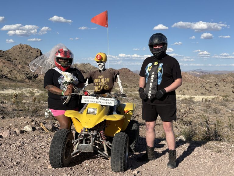 Las Vegas ATV tour: two riders by a yellow ATV with skeleton in veil; Nevada desert, mountains, blue sky in the background.