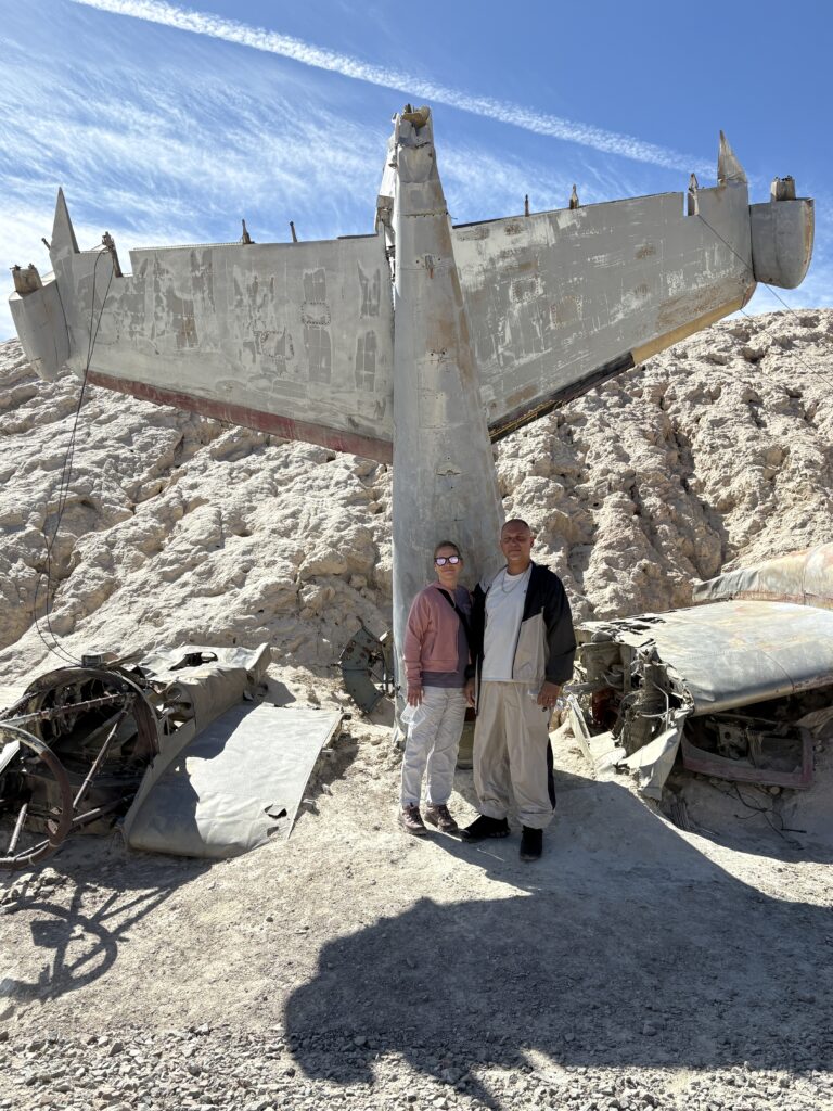 Smiling visitors by a weathered airplane wreck in Nevada’s rocky desert, near Las Vegas—ideal for ATV tours and Ghost Town sightseeing.
