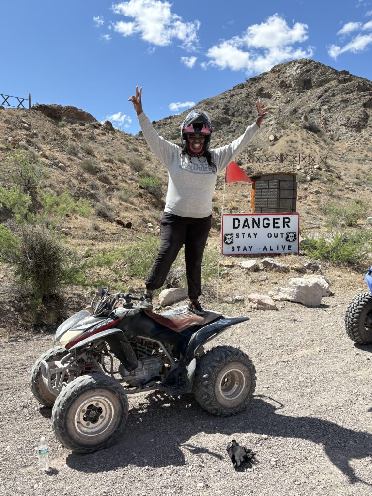 Rider raises arms on ATV in Nevada desert near Las Vegas, with DANGER sign. Great for ATV tours and RZR off-road rides.