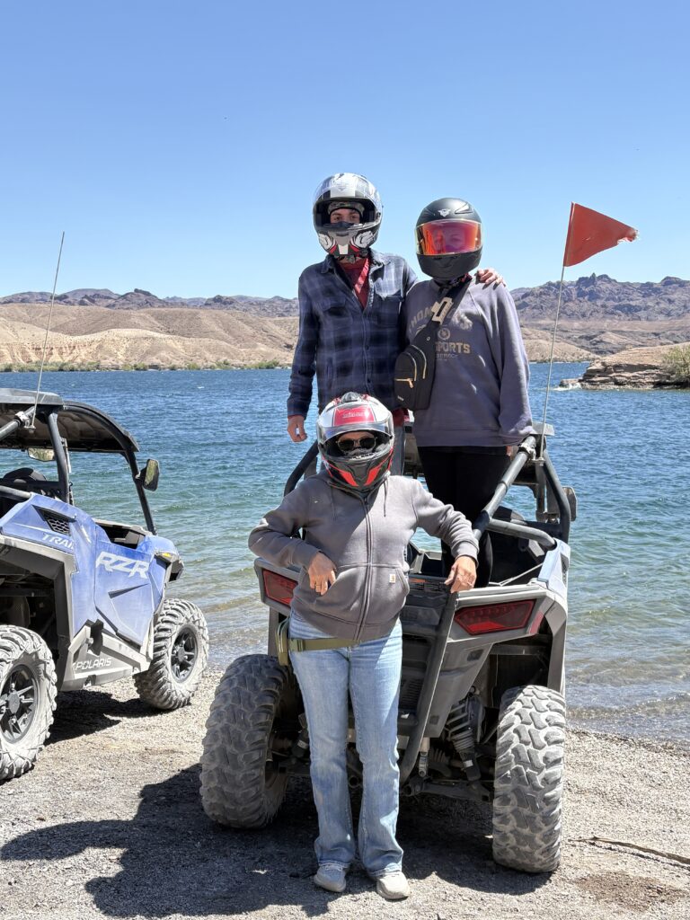Adventurers in helmets enjoy a RZR off-road ride by the Colorado River near Las Vegas, Nevada, with scenic mountains and ATVs.