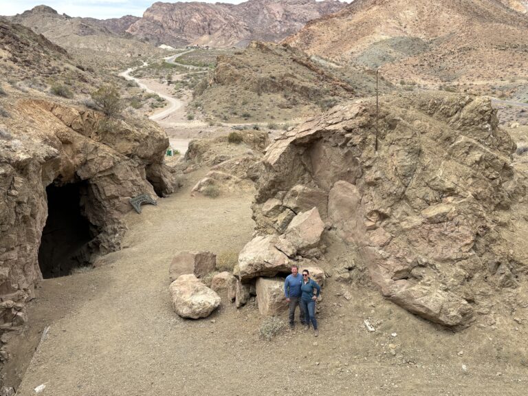 Adventurers near boulders and a cave in Nevada’s desert, with mountains and the Colorado River—ideal for ATV tours near Las Vegas.
