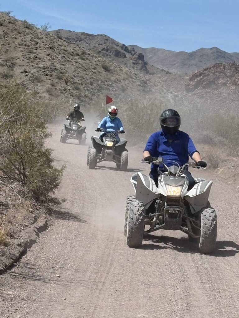 Adventurers on an ATV tour ride dusty desert trails near Las Vegas, Nevada, surrounded by rocky hills under a clear blue sky.