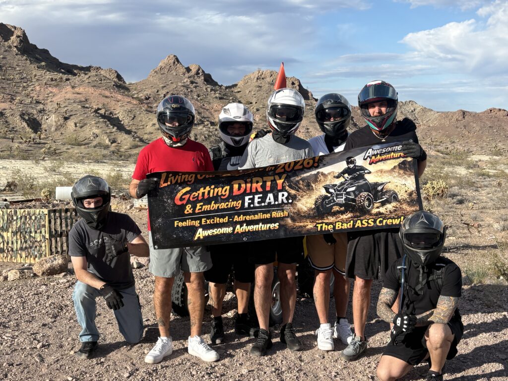Seven in helmets pose by Nevada desert, “Getting DIRTY & Embracing F.E.A.R.” banner, with Las Vegas ATV tour scenery behind.