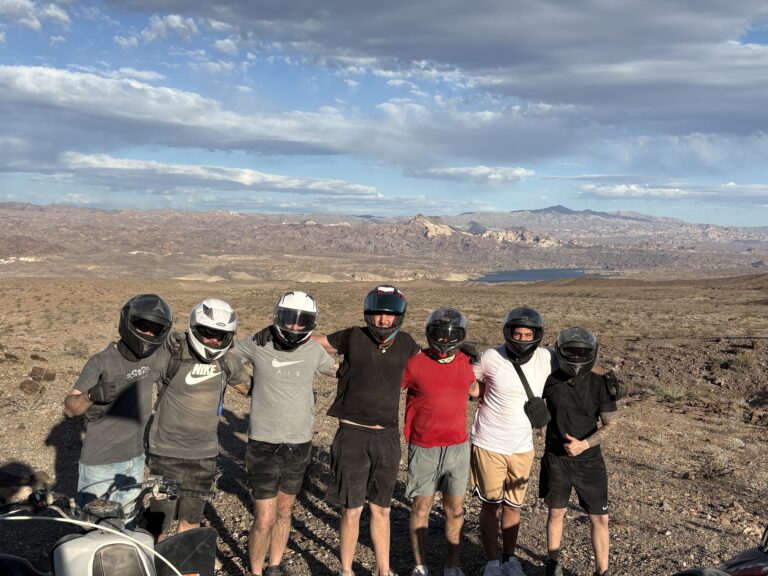 Group in helmets and casual wear stands on rocky Nevada desert near Colorado River, ready for Las Vegas ATV and RZR off-road adventure.