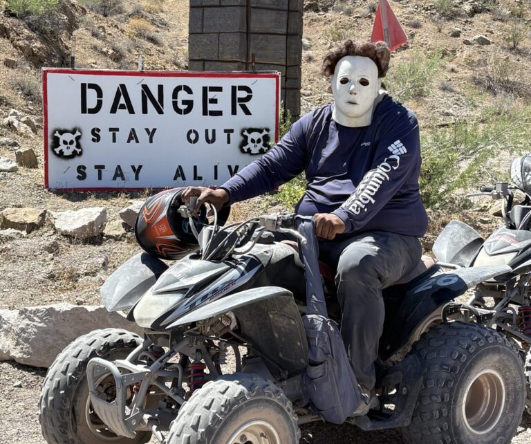 Rider in white mask on ATV near DANGER sign, rocky Nevada desert—perfect for Las Vegas ATV tours or Colorado River adventures.