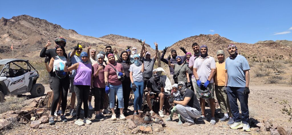 Group smiling in Nevada desert on an ATV tour near Las Vegas, giving thumbs up by off-road vehicle under clear blue sky.