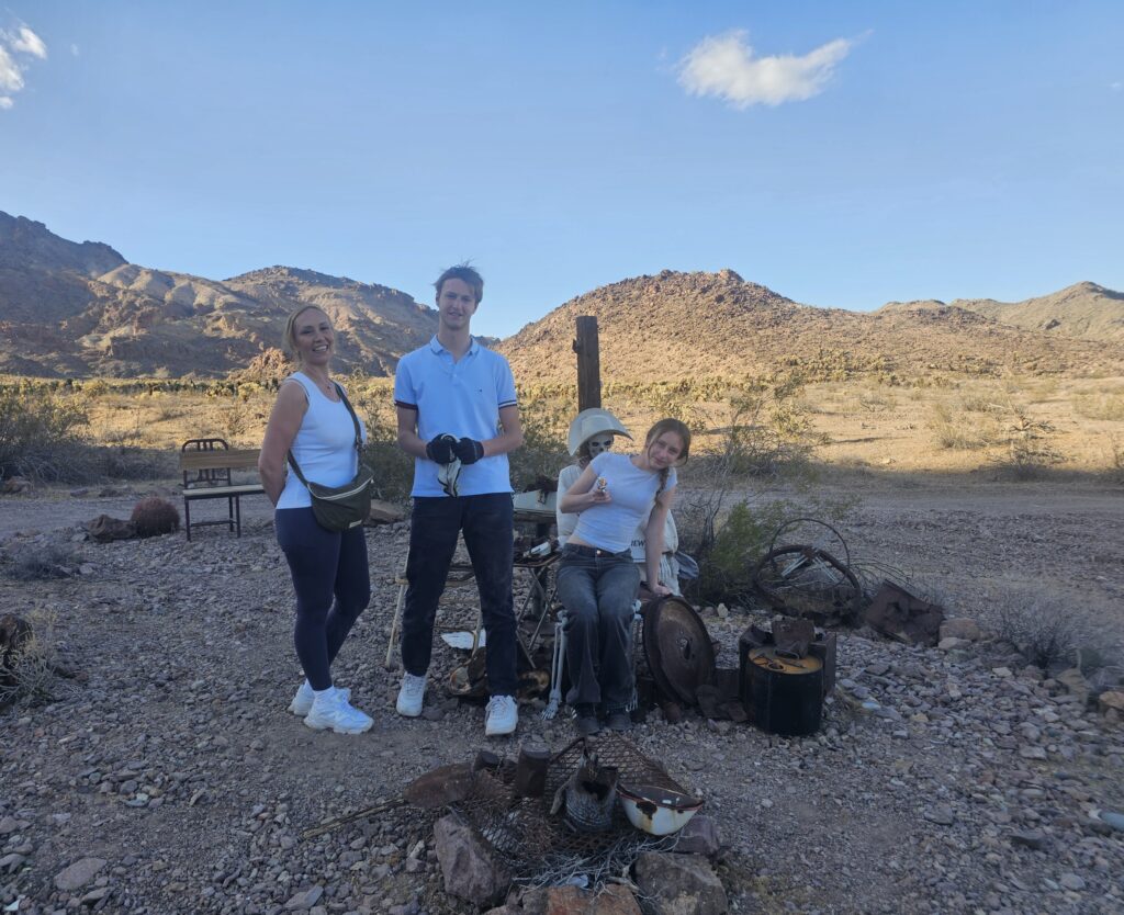 Smiling group by Nevada’s rocky desert near Las Vegas; wheelchair user, metal relics, and ghost town sightseeing backdrop.