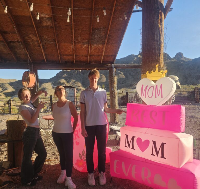 Three people smile by a “Best Mom Ever” display at a rustic Nevada mountain shelter, perfect for Las Vegas ATV or RZR tours.