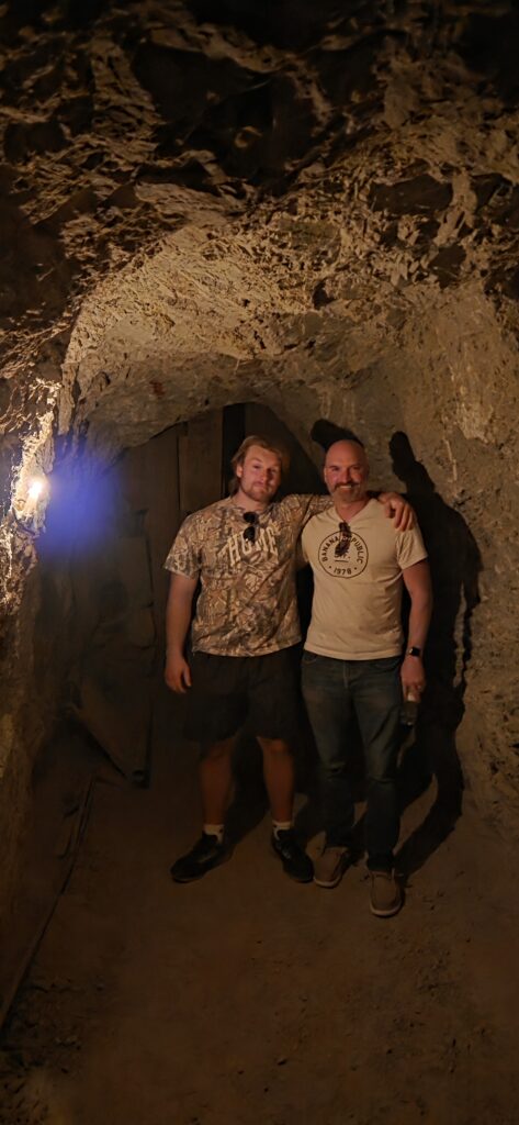 Two men in a rocky Nevada cave, illuminated by a single bulb—perfect for Las Vegas ATV tours or Colorado River adventures.