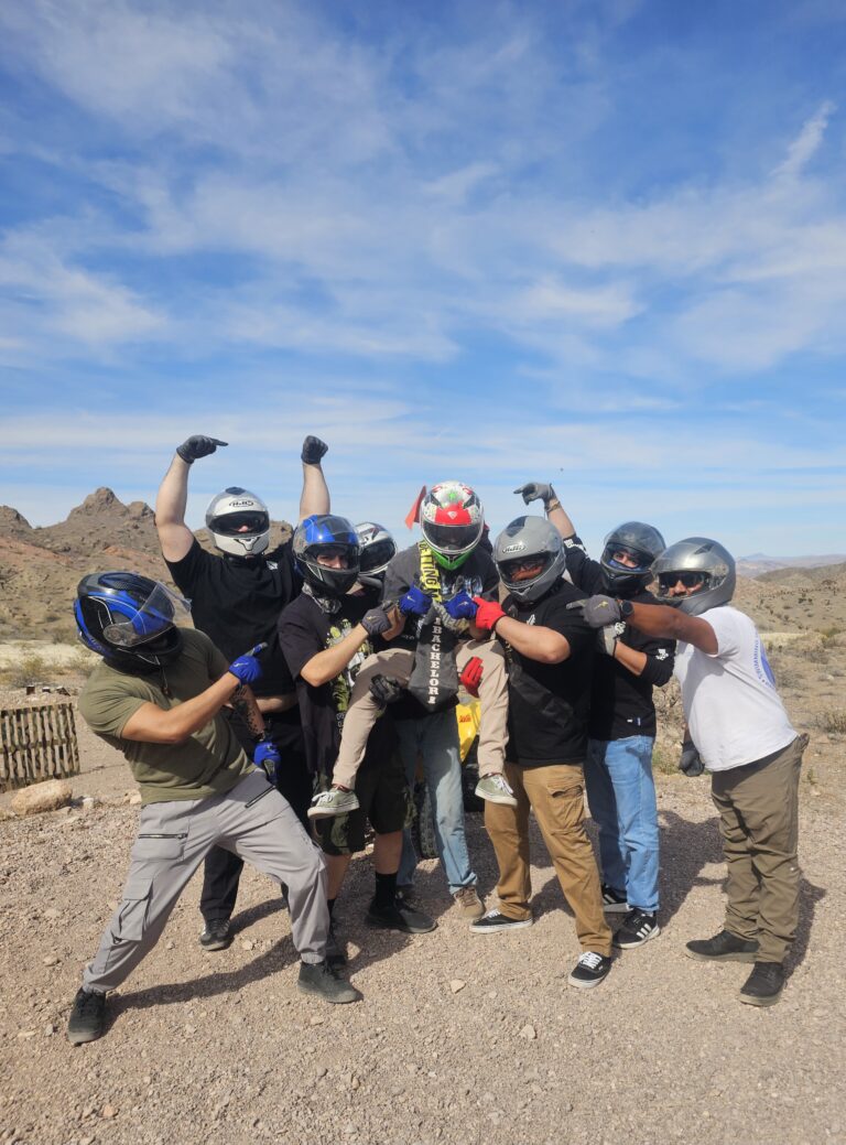 Group in helmets celebrates with trophy during Nevada ATV tour near Las Vegas, desert hills and blue sky in the background.