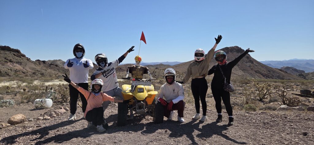 Group poses with arms raised by a yellow ATV on a Nevada desert tour near Las Vegas, rocky hills and blue sky behind.