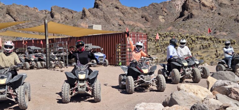 Group on ATVs with helmets in Nevada desert near Las Vegas, ready for an ATV tour by rocky hills and shade tents.