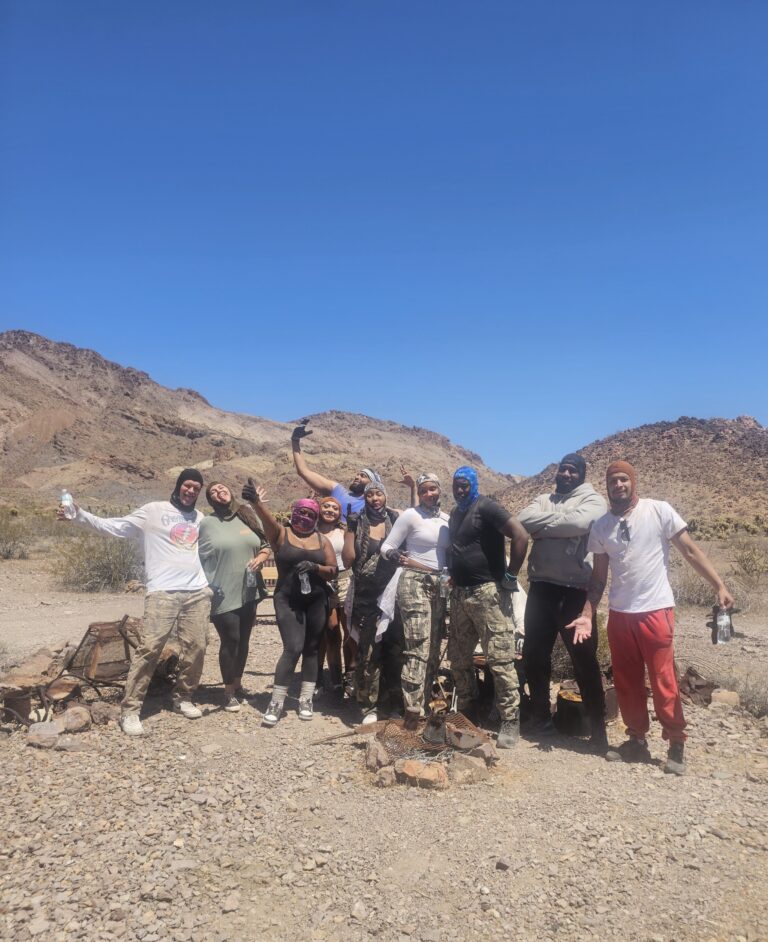Group of eight poses playfully in Nevada desert near Las Vegas mountains, dressed for ATV tours or Colorado River RZR adventures.