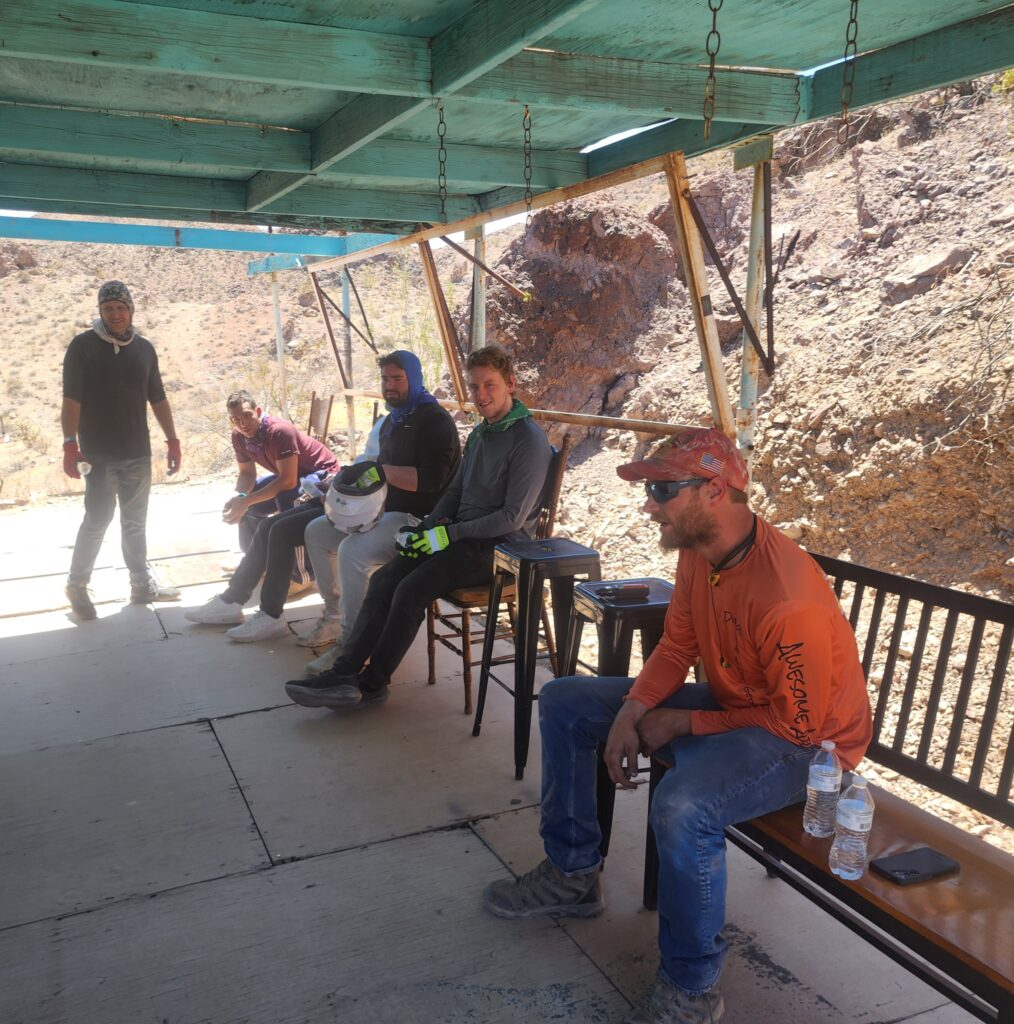 Group relaxing under shaded spot in Nevada desert near Las Vegas, water bottles on bench after RZR off-road tour.