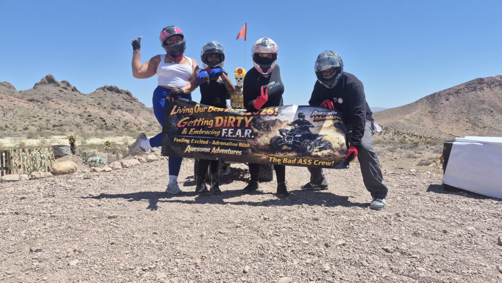 Group in helmets and off-road gear hold “Getting DIRTY & Embracing F.E.A.R.” banner on a Nevada ATV tour near Las Vegas.
