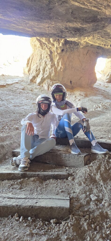 Smiling duo in helmets on wooden steps inside a sunlit Nevada cave, perfect for Las Vegas ATV tours or Ghost Town sightseeing.