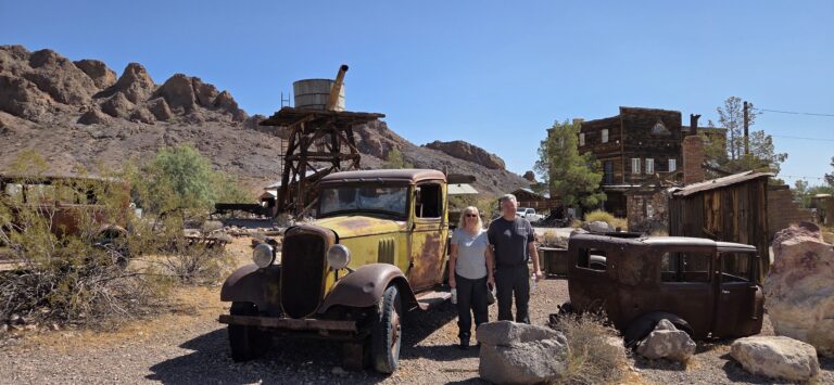 Visitors stand by a rusty vintage car in a Nevada desert ghost town near Las Vegas, ideal for ghost town sightseeing tours.