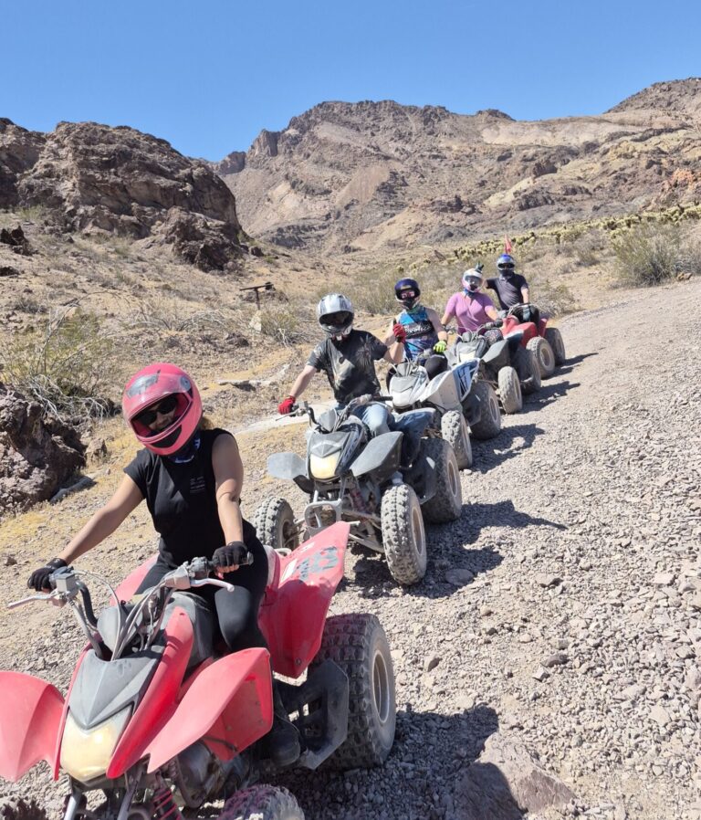 ATV tour near Las Vegas: four riders on rocky desert trail, pink helmet in front, clear sky, Nevada mountains in background.