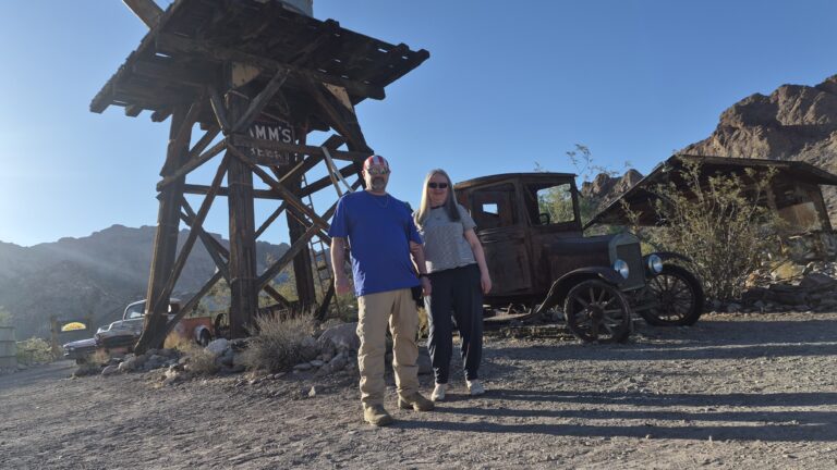A couple stands under a wooden water tower by a rusty car in Nevada desert near Las Vegas, perfect for Ghost Town sightseeing.