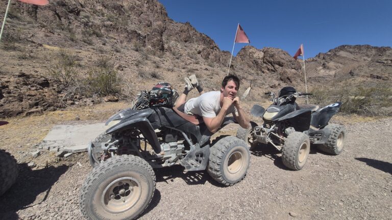 Smiling rider lies on ATV during a thrilling Nevada desert tour near Las Vegas, with rocky mountains and blue sky behind.
